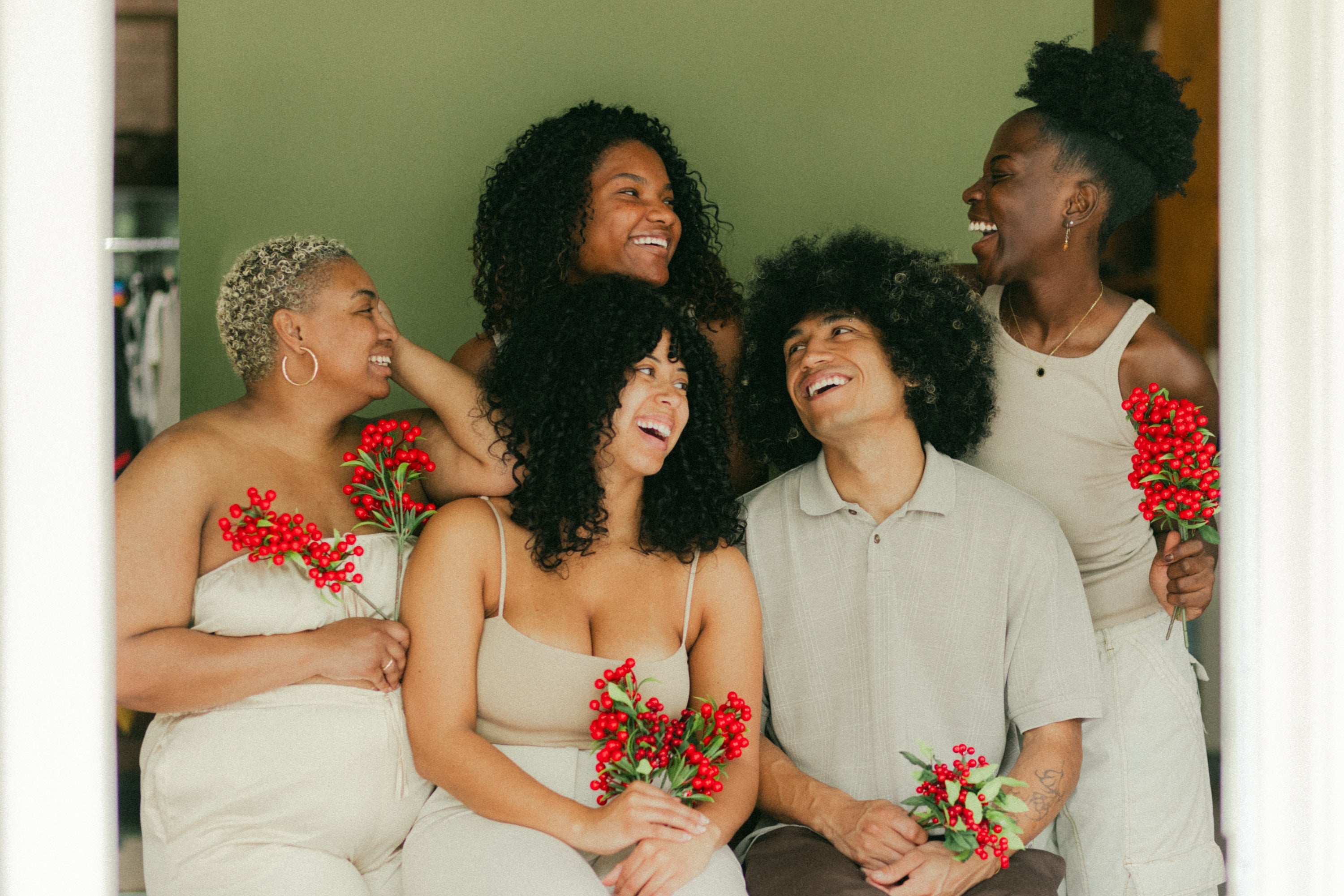 Five smiling adults wearing white and beige clothing and holding branches with red berries on a green background.