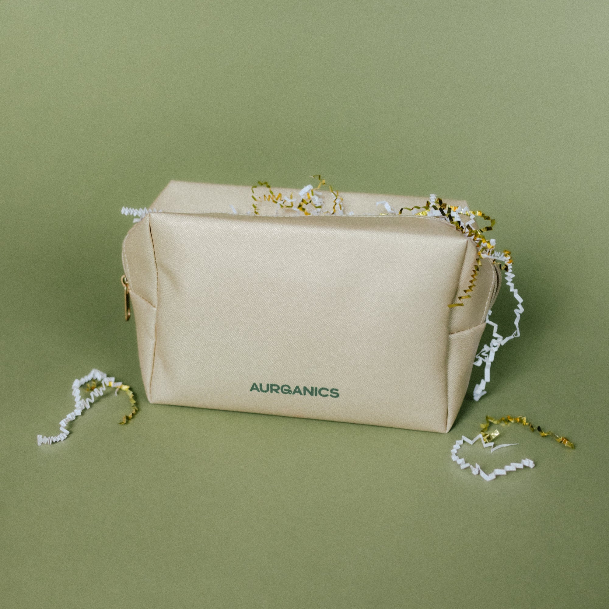 Gold cosmetic bag with AURGANICS branding on a green background by AURGANICS skincare for melanated glow-getters