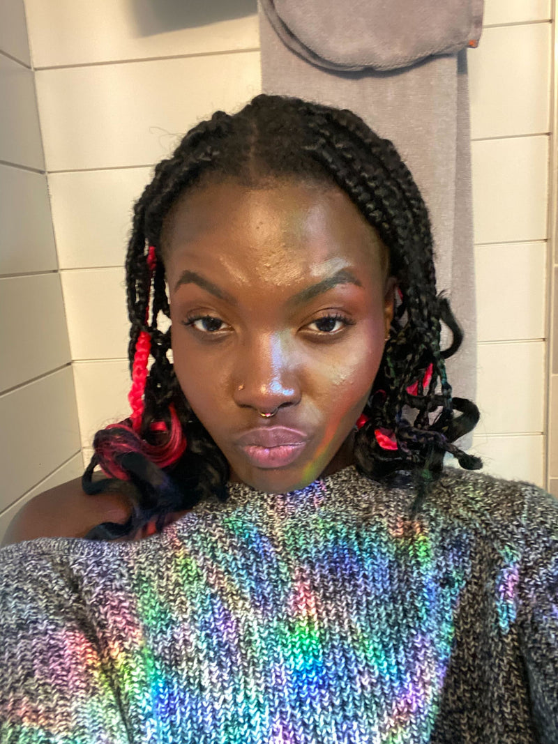 Person with braided hair wearing a colorful sequin top in a bathroom setting