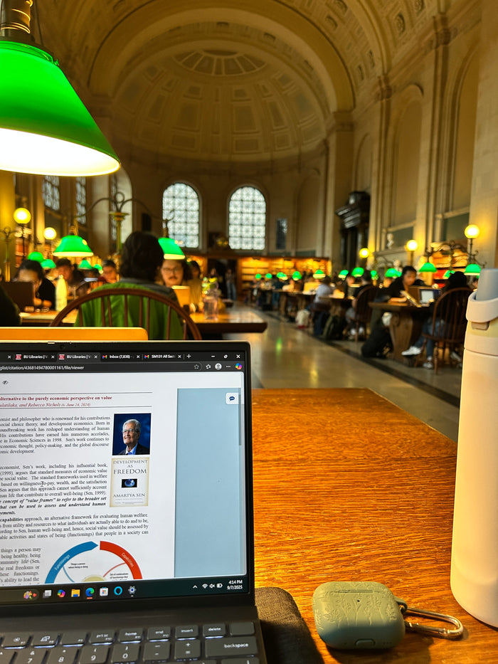 Laptop on a table in a library with people studying in the background